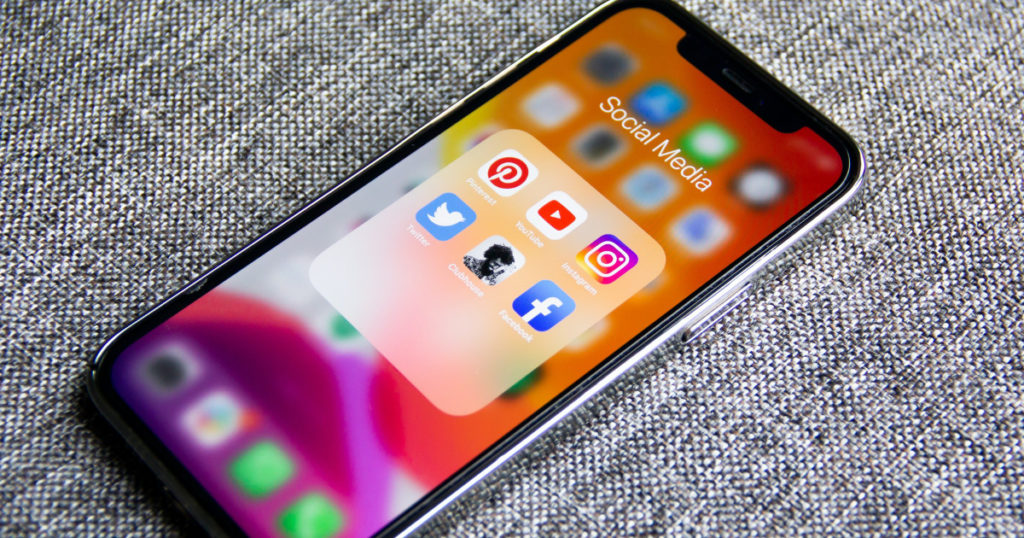 A smartphone with the with the social media folder open. Pinterest, YouTube, Instagram, Twitter, Facebook and one other app is on the screen.