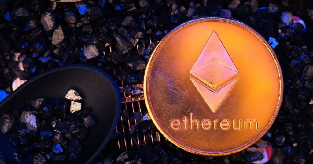 A physical coin, with the Ethereum logo and text on it, sitting on top of what looks to be obsidian pieces.