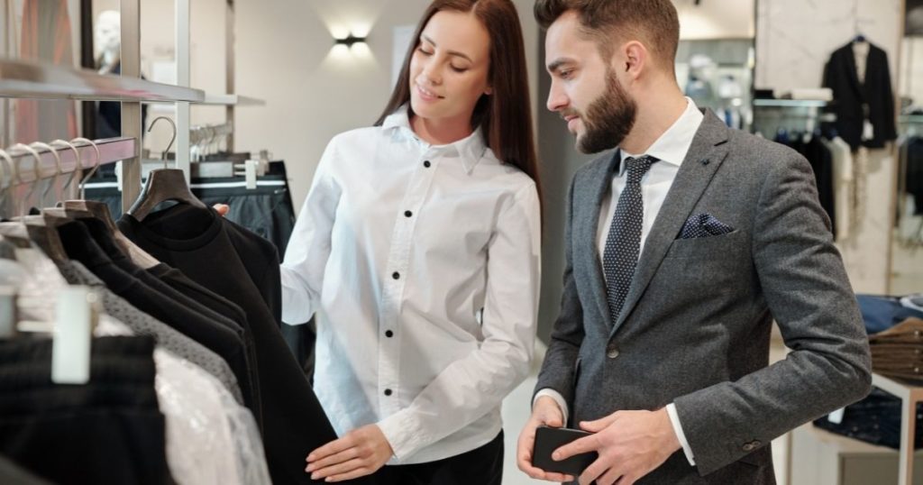 kadın bir moda danışmanı erkek müşterisine iş kıyafeti seçmesinde yardımcı oluyor.