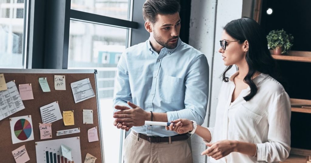 find a product to sell online , two people talking near a board.